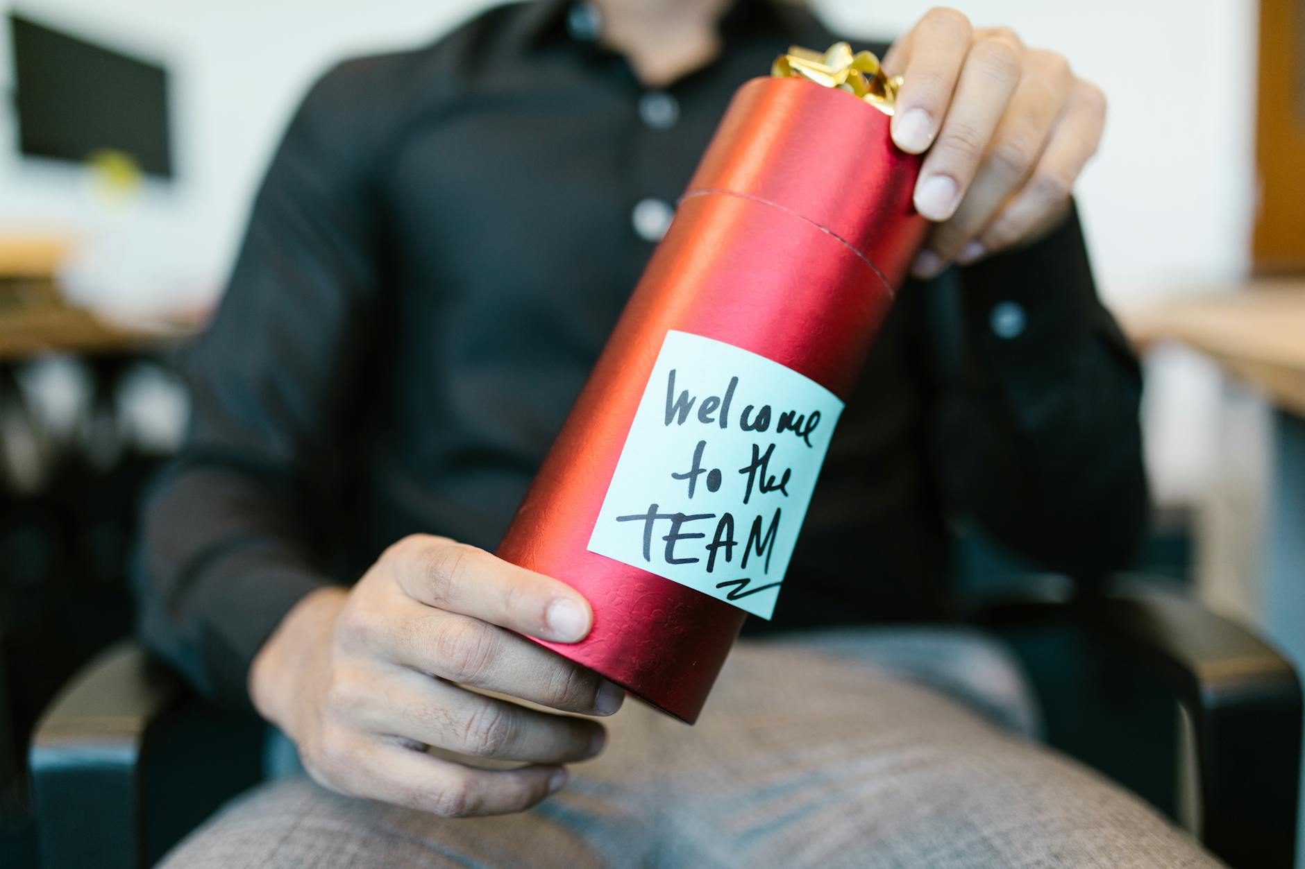 Czerwane pudełko prezentowe z kartką welcome to the team w dłoniach