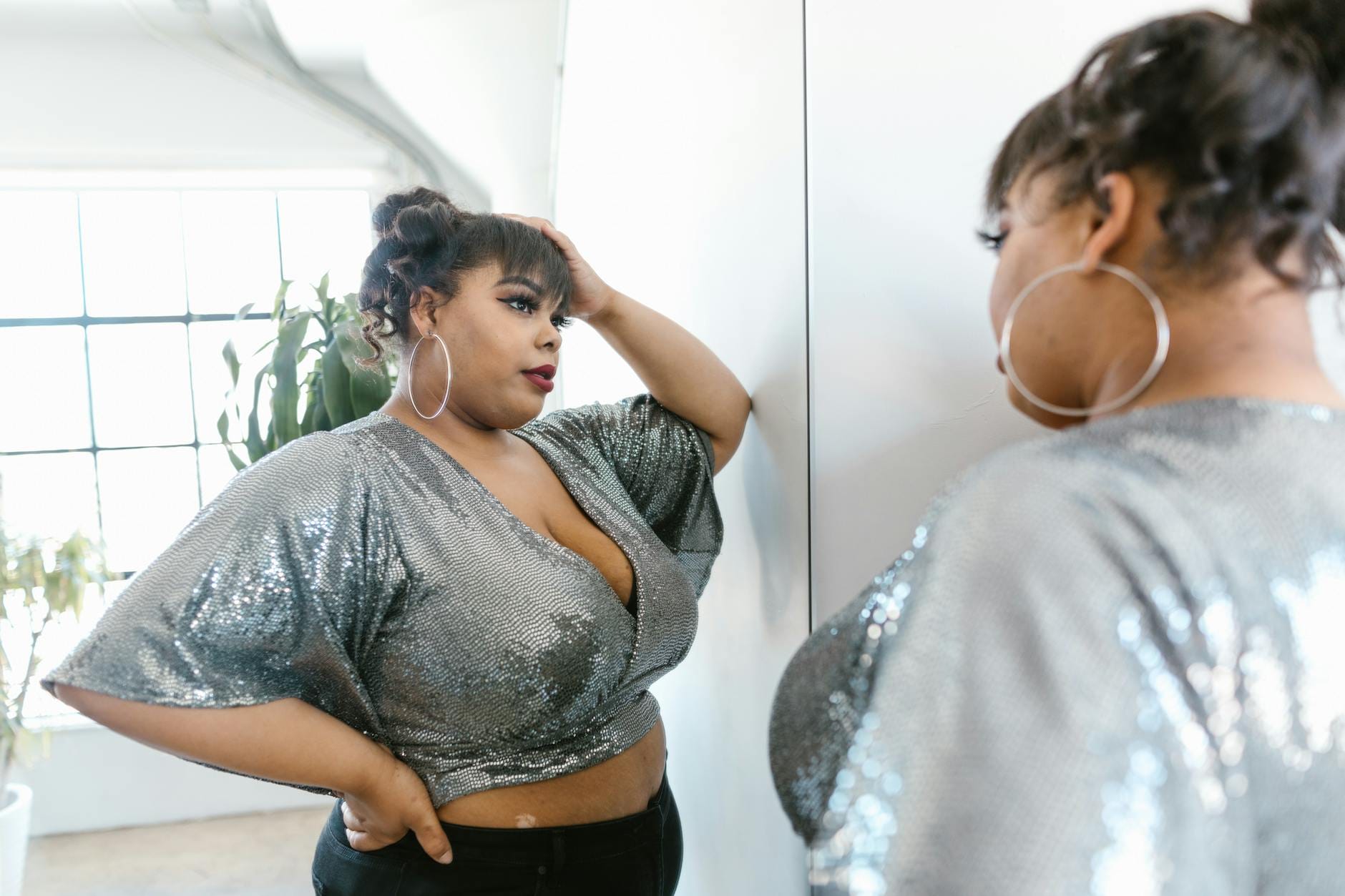 Pewna siebie kobieta plus size w błyszczącej bluzce pozuje przed lustrem