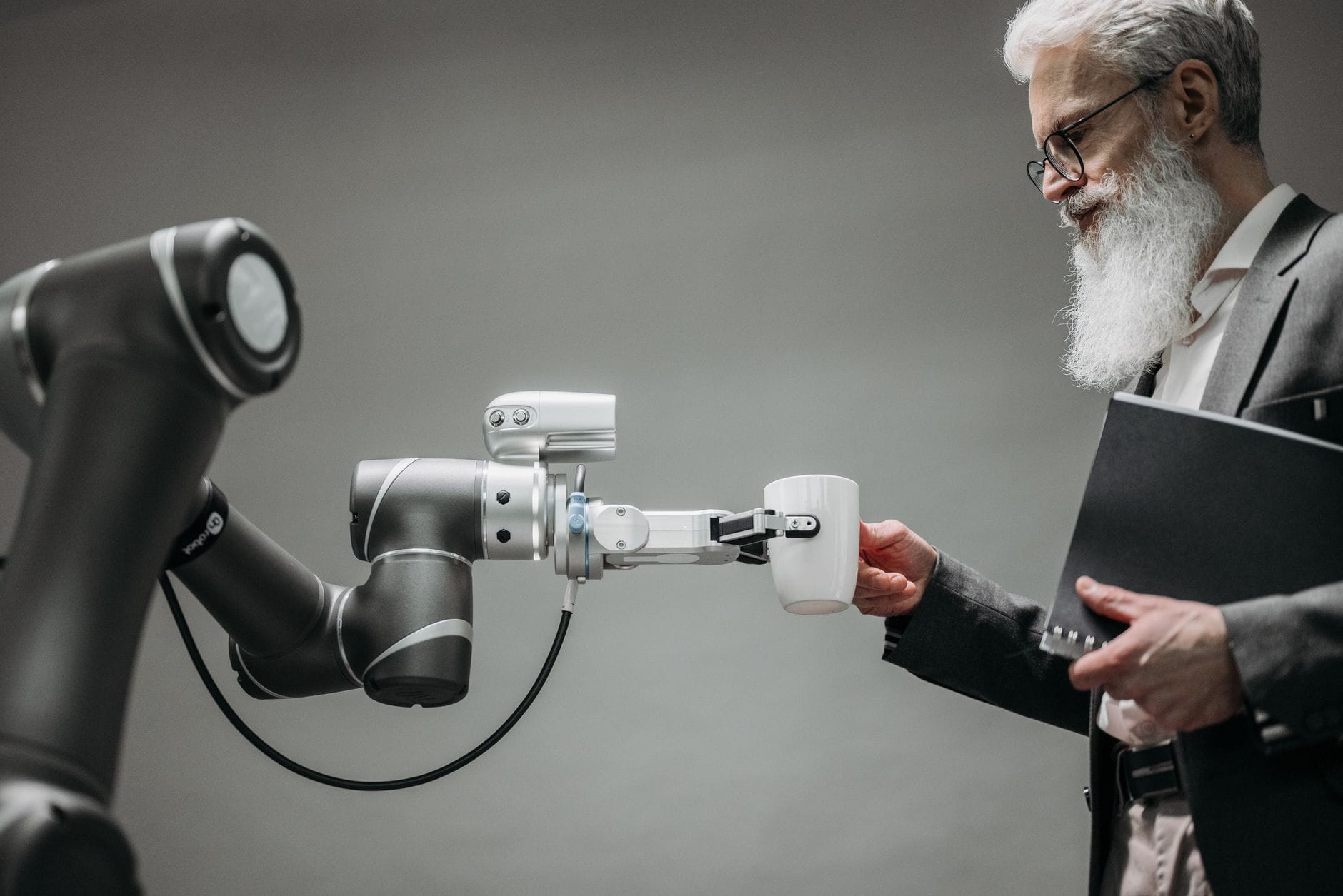 Starszy mężczyzna odbiera kubek od robota w nowoczesnym biurze