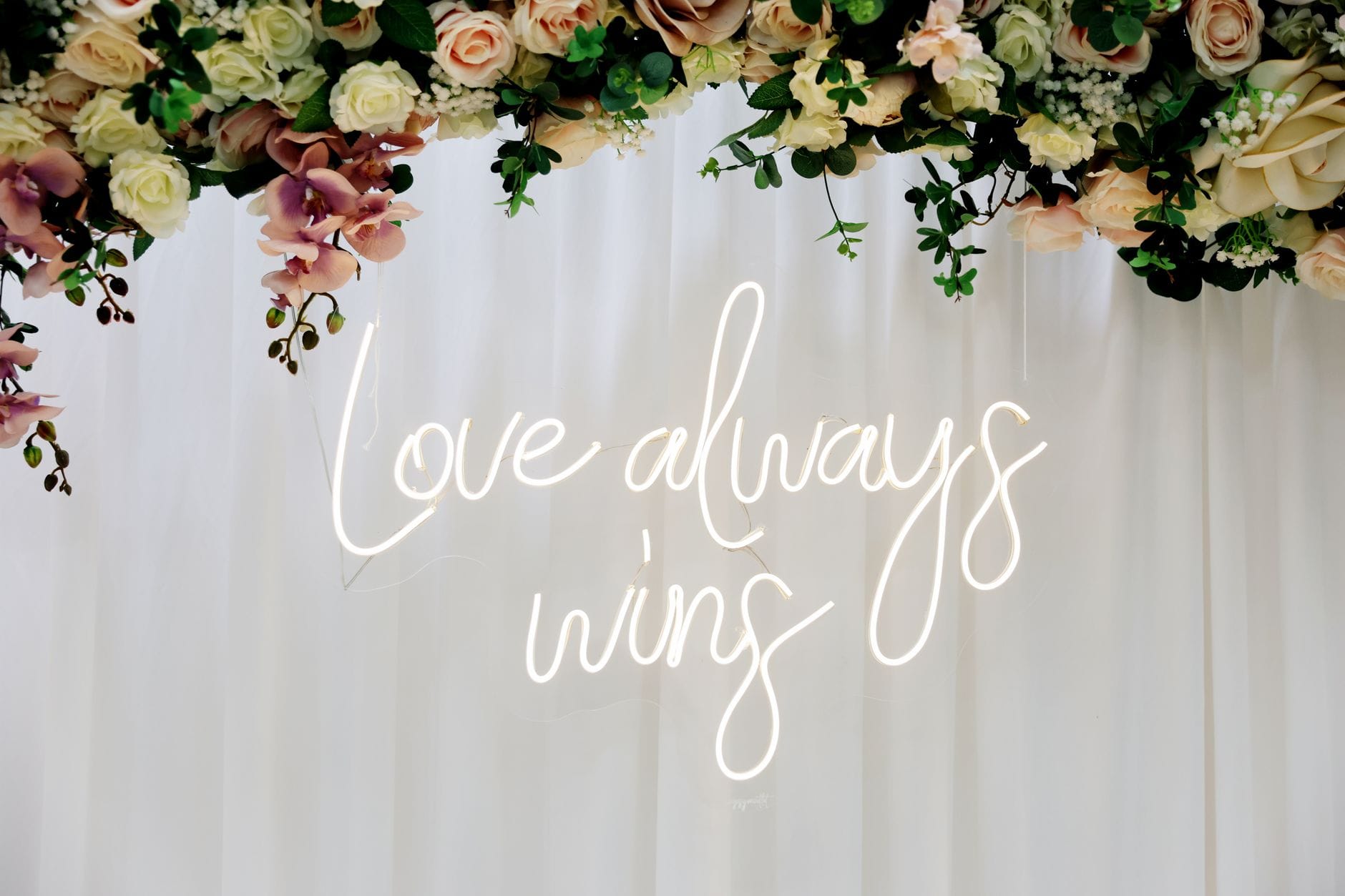 Kompozycja kwiatowa z neonowym napisem Love always wins na weselu